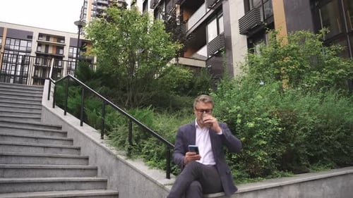 Smiling Man Using Mobile Phone and Drinking Coffee in the City Real Time Concept
