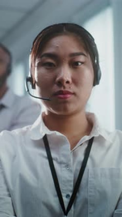Ernsthafte asiatische Hotline-Betreiberin mit Headset blickt in die Kamera