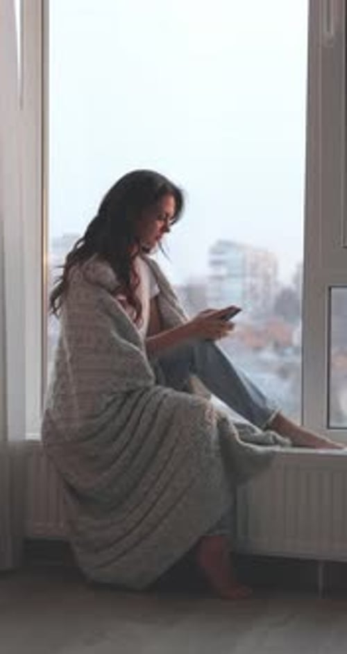 Woman Wrapped in Blanket Using Mobile Phone Indoors