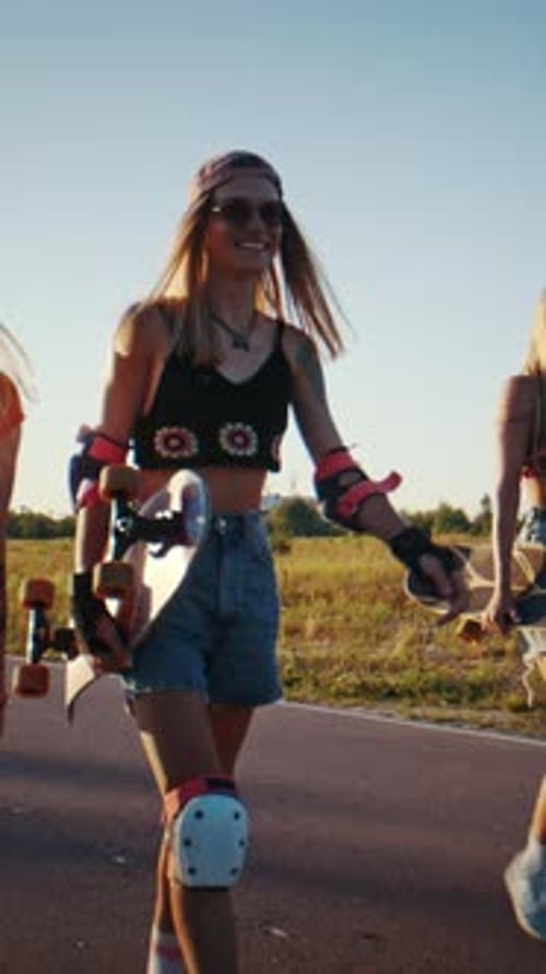 Women Friends Carry Skateboards and Stroll Along Paved Road
