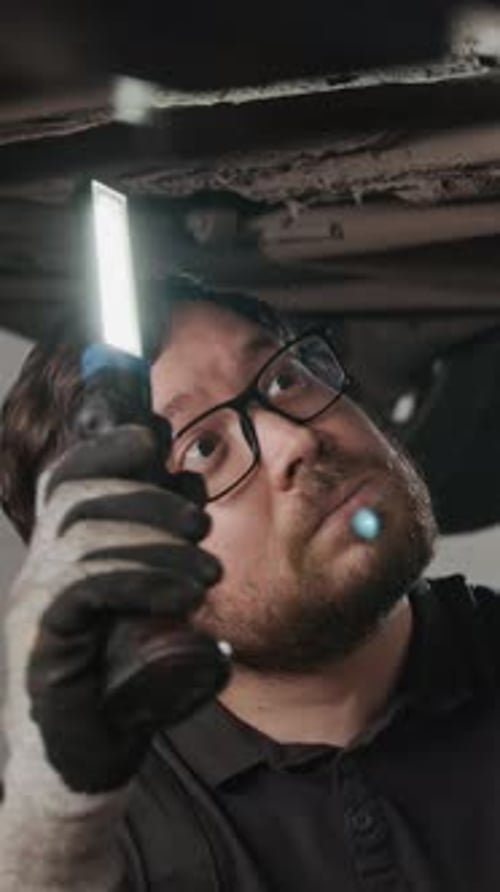Vertical of Mechanic with Torch Inspecting Undercarriage of Car on Lift
