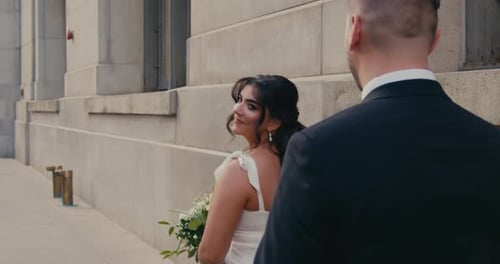 A Closeup Shot From Behind the Bride Walking Forward with the Groom Following Her on a City Street