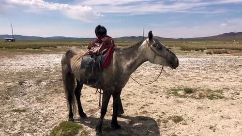 Asian male climbs up into saddle on horse and rides away on the Mongolian steppe