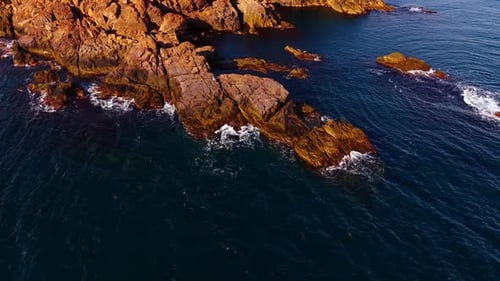 Approaching to the bare rocks lit by the bright sun. Waves splash by the rocky shore.