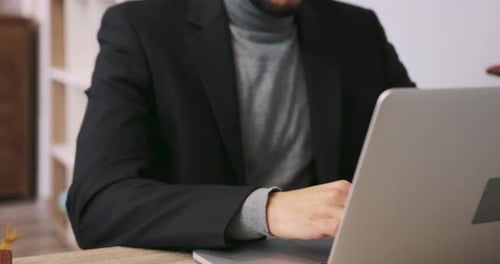 Vista de perto de um homem sério em um traje formal usando ativamente seu laptop digitando mensagens do que ele