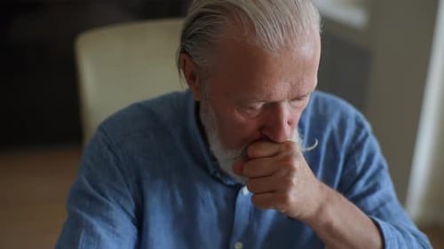 Senior Man Coughing into Hand in Interior Setting