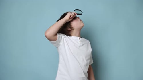 Little boy with magnifying glass on light blue background