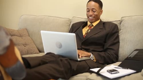 Man In Suit Working From Couch With Laptop
