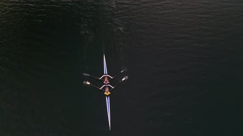 Top View of a Sports Rowing Boat with Two Women Rowing Off on Calm Water