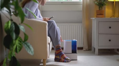 Eine hübsche junge Frau schaltet einen modernen Luftbefeuchter im Wohnzimmer ein