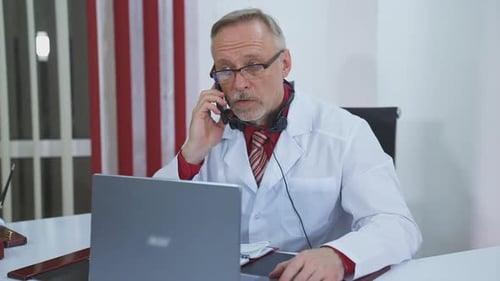 Doctor on Phone With Laptop in Office
