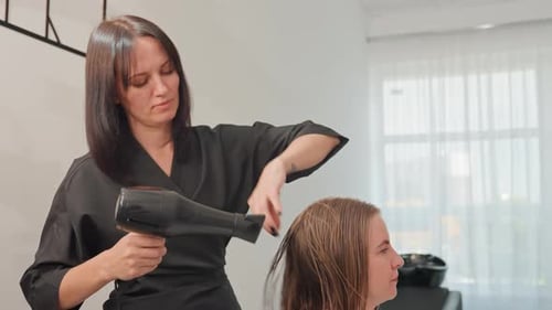 Woman Hairstylist Dries Client's Hair with a Hairdryer