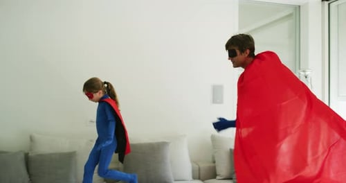A carefree happy father and daughter dressed as superheroes are having fun to run and jump while p