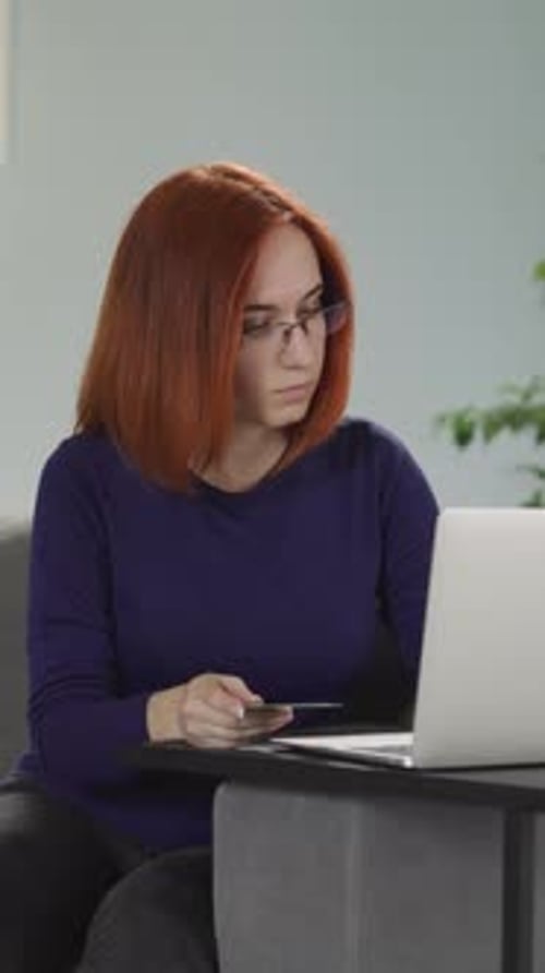 Redhaired Woman in Glasses Enters Card Details Into Laptop