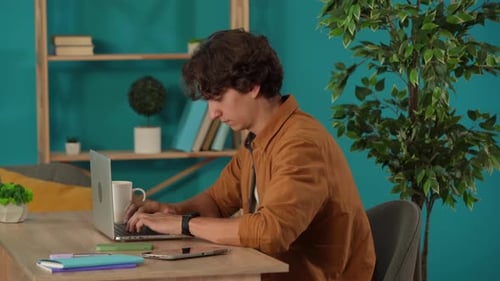 Medium Shot Capturing a Man Working on a Laptop in His Home Office and Drinking Coffee Young Male
