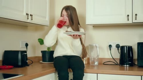 Girl Eats Cake and Drinks on Kitchen Counter