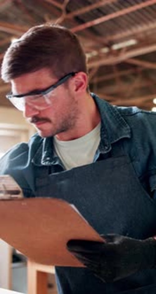 Carpenter, clipboard and man in workshop, writing and checklist for inventory