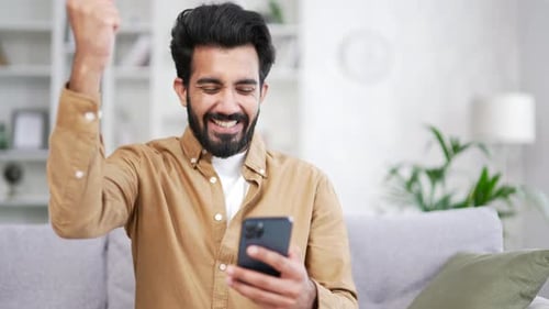 Close up Happy young man received great news on smartphone while sitting on sofa in living room
