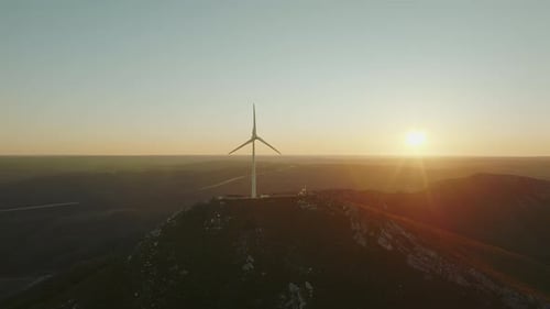 Large windmill on top of the mountain at beautiful golden sunset. Alternative energy production.