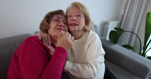 Two senior women embracing, showing genuine love and affection while sitting together on a couch. An