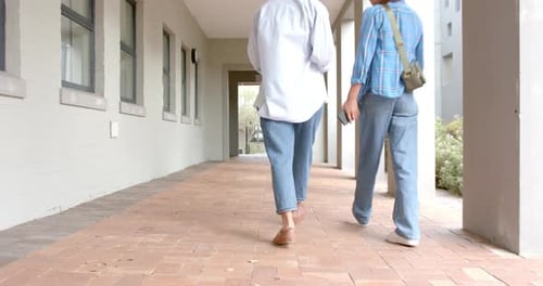 Walking in high school hallway, students carrying books and backpacks, heading to class