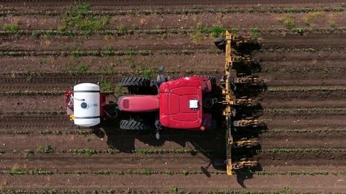 Tractor que tira del brazo de descarga de fertilizantes a cámara lenta sobre cultivos frescos