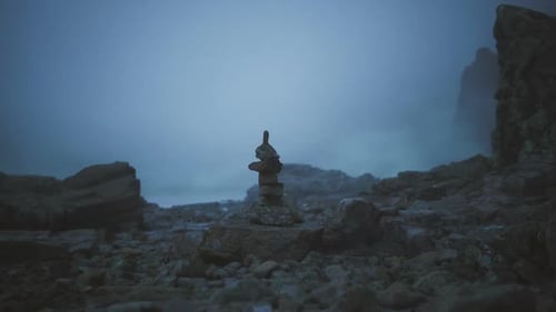 Rock Balancing on a Rocky Shore During a Foggy Day