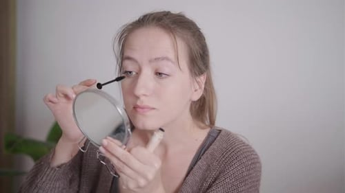 Woman Applying Mascara with Handheld Mirror at Home