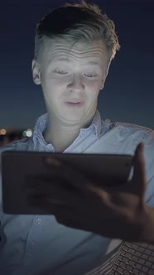 Un jeune homme sourit joyeusement à son appareil tout en profitant d'un magnifique paysage urbain nocturne
