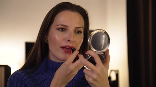 A Young Caucasian Woman Applies Lipstick and Smiles at Herself in a Pocket Mirror in an Apartment
