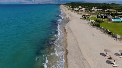 Aerial Drone Flies Along Long Sandy Beach with Turquoise Water, Sunbeds, and Coastal Village