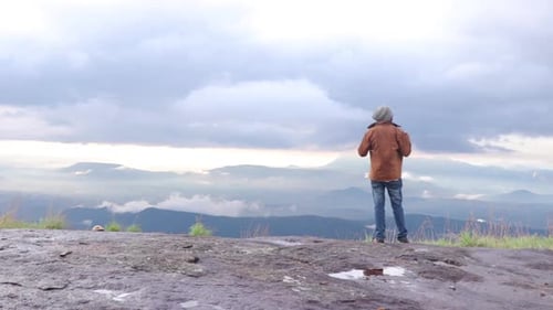 Young man standing on top of cliff enjoying view of nature.