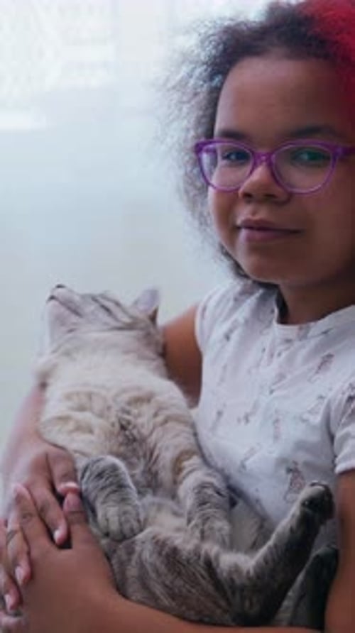 Girl Cradling a Cat Indoors near a Window