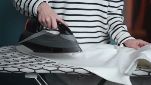 Woman Irons Clothes on an Ironing Board in the Laundry Room at Home Closeup