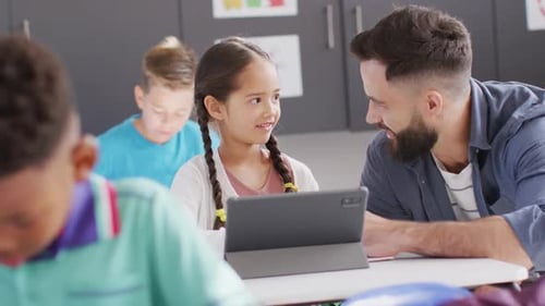 Diverse male teacher and happy schoolchildren using tablet in school classroom