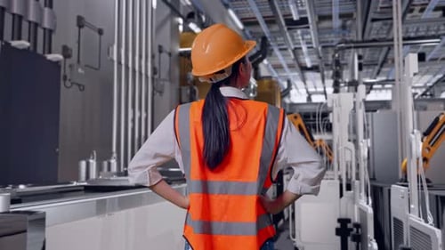 Vue arrière d'une ingénieure debout avec des bras Akimbo, usine de batteries