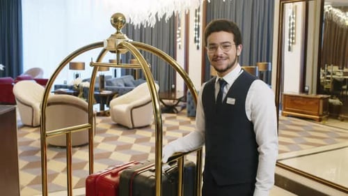 Young Porter Standing next to Cart with Clients Suitcase