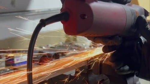 A close-up of a person using a powered metal saw to cut a screw, causing orange sparks to fly. The c