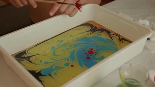 Manos de niños rociando pintura sobre el agua en el arte tradicional de marmoleado de Ebru