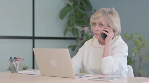 Senior Woman Working at Desk on Laptop and Phone