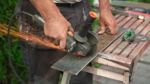 Worker cutting metal tube using an Angle Grinder. Bright sparks and flashes