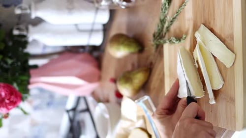 Young female hands are cutting cheese on a wooden plank close-up. Cooking concept. Vertical footage