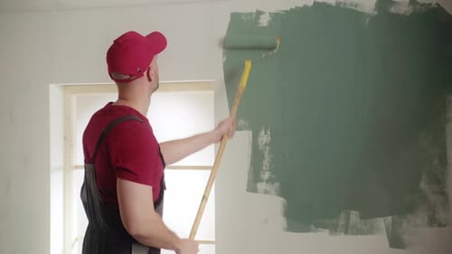Painter Skillfully Applying Green Paint to Wall