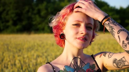 Portrait of Happy Punk Girl with Pink Hair with Blurred Wheat Green Field at Background Carefree
