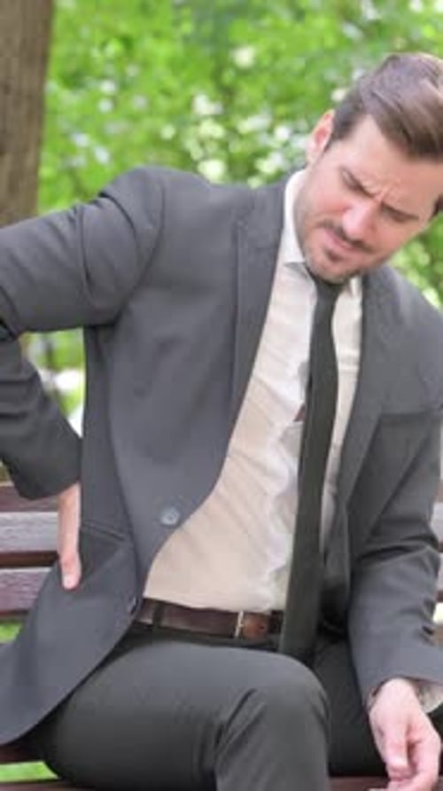 Man in Suit Massaging Sore Back on Bench