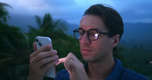 Young Adult Uses Phone At Night In Tropics