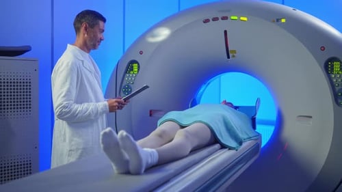 Medical Worker Standing Confidently Near MRI Tunnel While Female Patient Resting on Table Overseeing