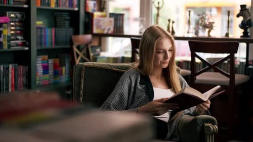 Closeup in a Beautiful Bookstore a Young Girl with Long Hair Sits in a Chair Reading a Book Evening