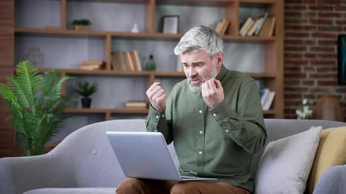 Man Sitting on Sofa Using Laptop Expressing Frustration