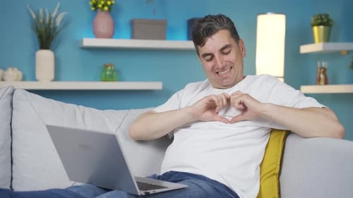 Happy Man Video-Calling From Couch Making Heart Symbol